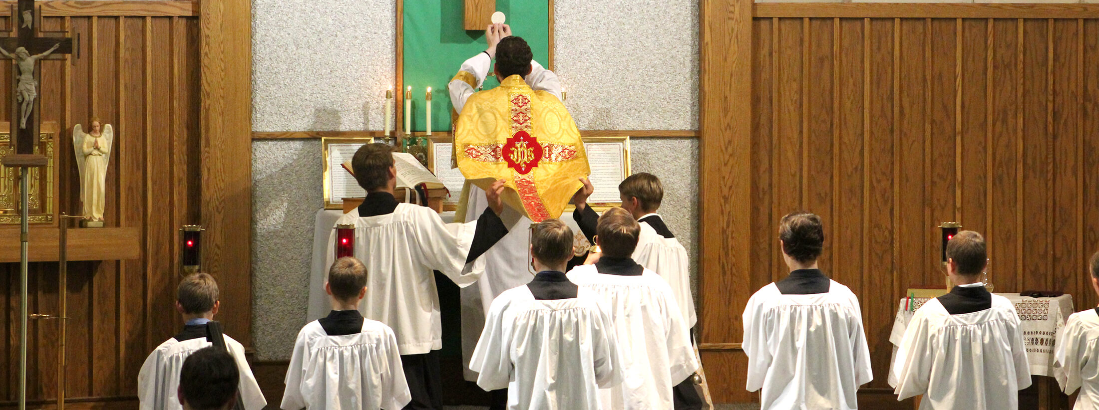Father holding up the Holy Eucharist to the cross with altar boys behind him