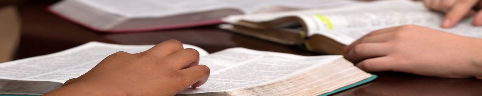 Open bibles sitting on a table with young hands reading the scriptures