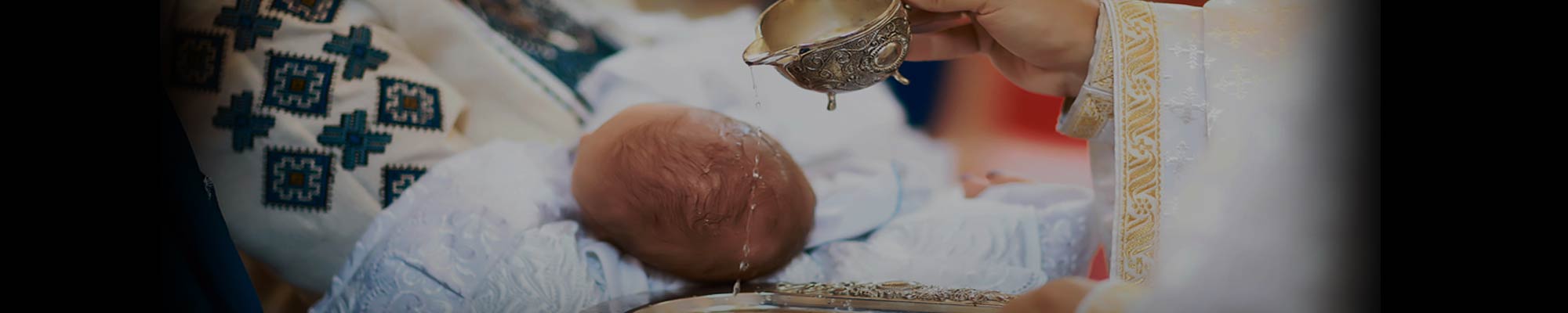 Newborn baby wrapped in light blue cloth receiving the sacrament of baptism