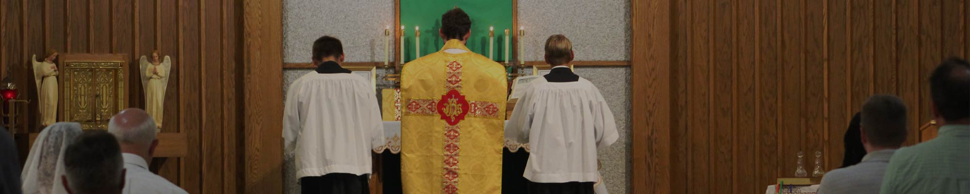 Catholic priest with two altar boys kneeling at the foot of the cross inside St. Johns Cantius Church